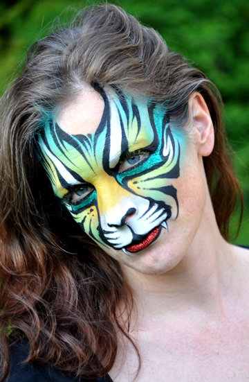 woman with a tiger face painting that resembles a tiger with green and yellow colors